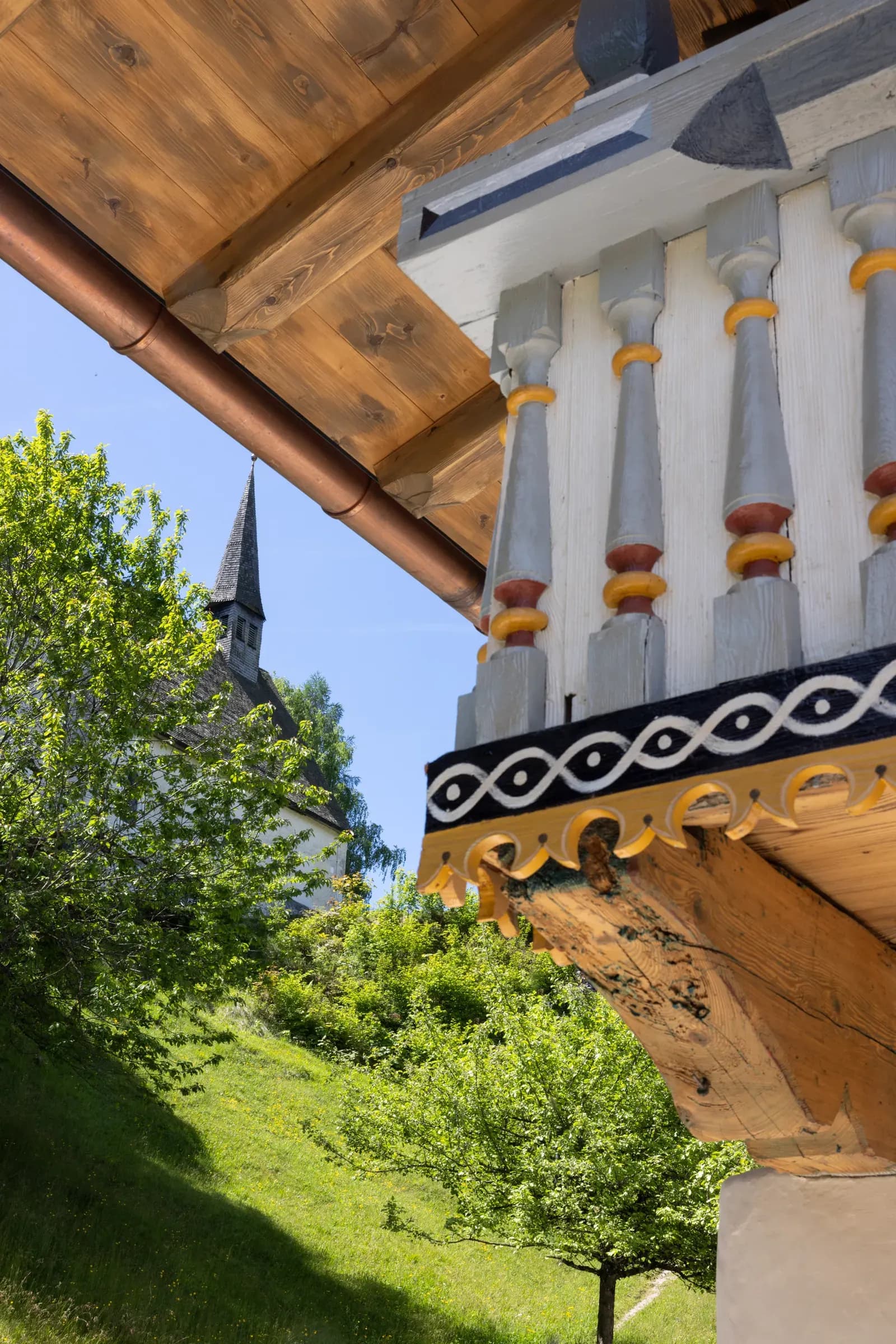Verzierter Balkon am Berggasthof Streichen mit Blick auf den Turm der Streichenkirche